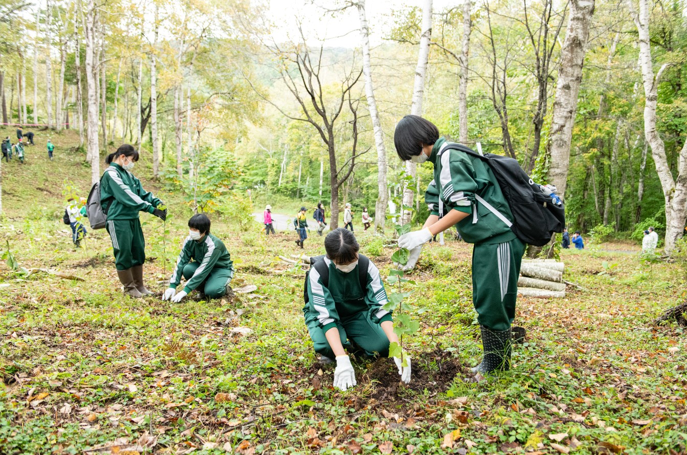 緑色のジャージを着た学生たちが植樹を行っている写真