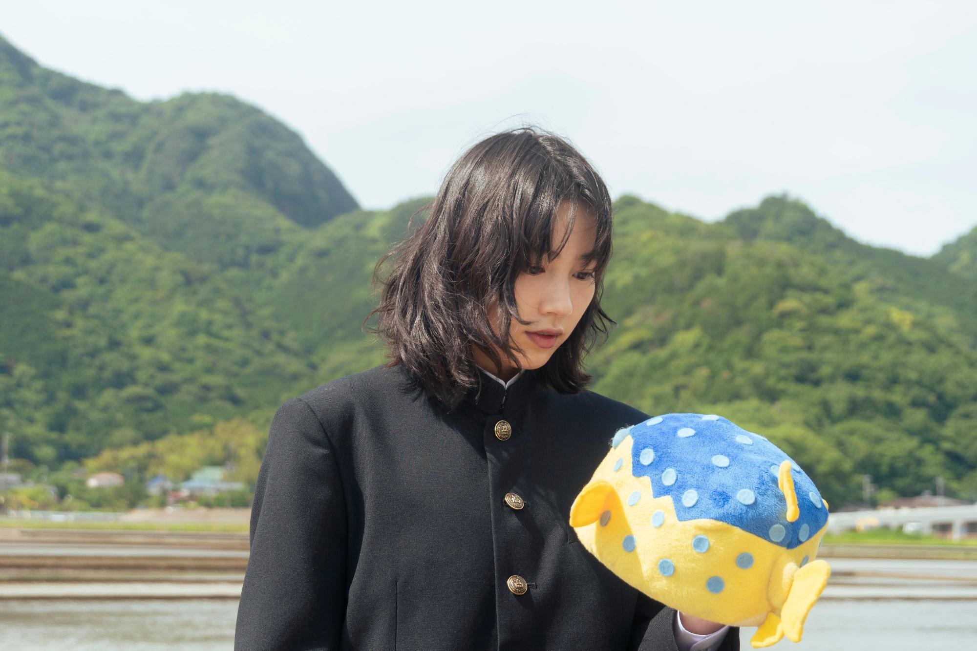 男子学生服を着た女性が魚の形の帽子を持っている写真