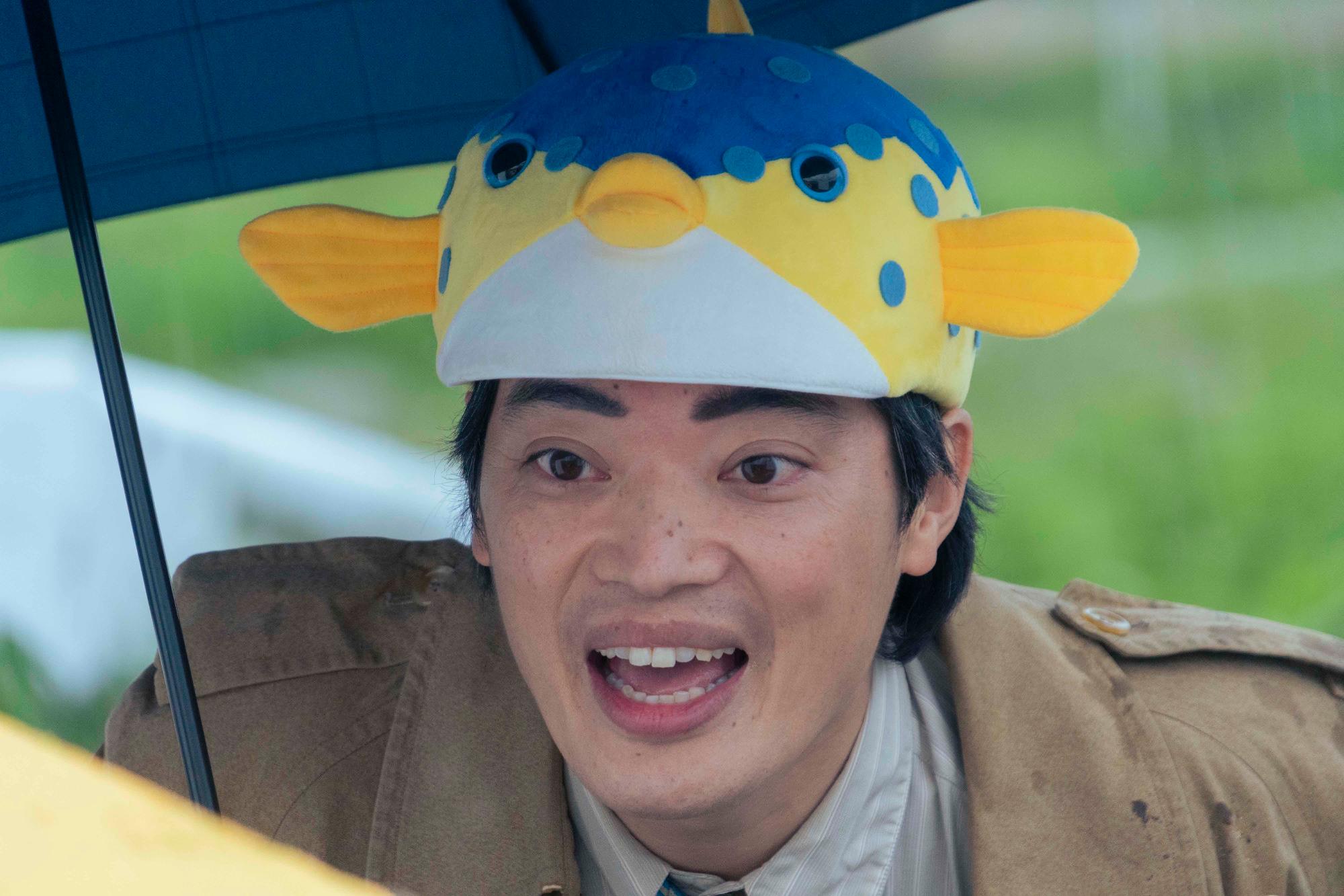 魚の形の帽子をかぶった男性が傘を持っている写真
