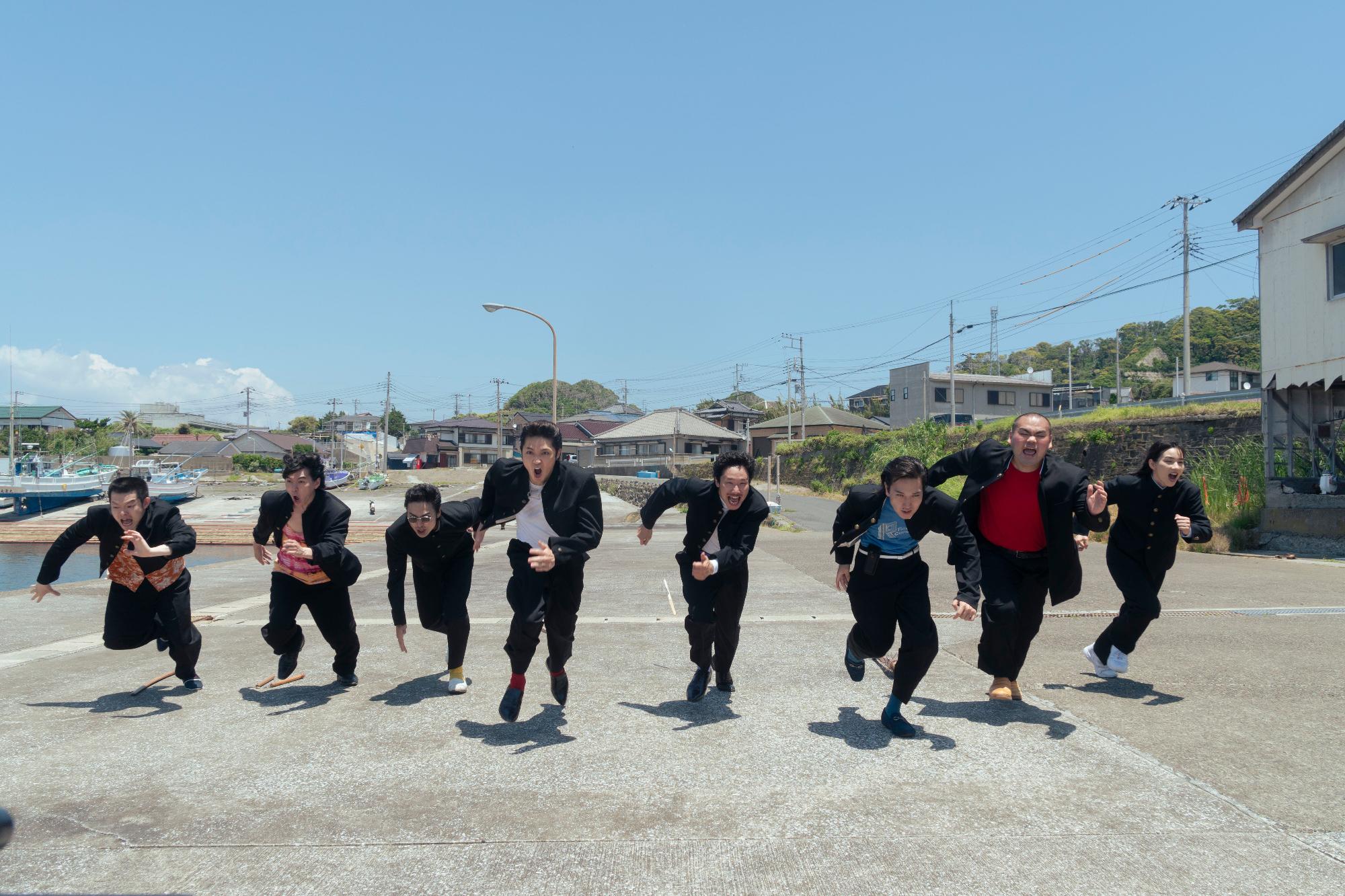 男子学生服を着た7人の男性と1人の女性が屋外で走っている写真