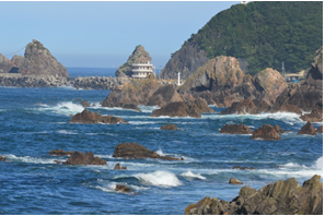 荒々しい岩の点在する海の奥に小さの建物が見えている写真