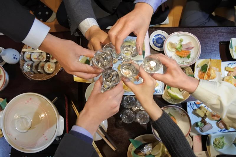 複数の料理が並んだテーブルの上で乾杯している手元の写真