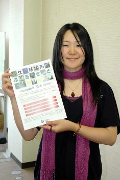 紫色のストールを首に巻いた髪の長い女性がパンフレットを持っている写真