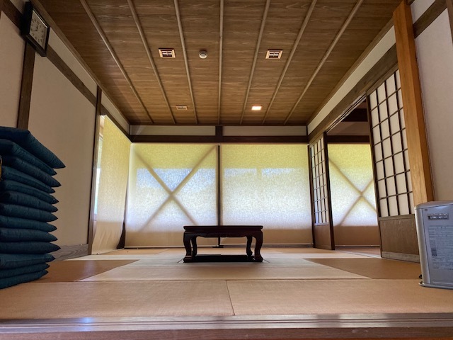 積み重なった座布団や小さい机が置かれている和室の写真