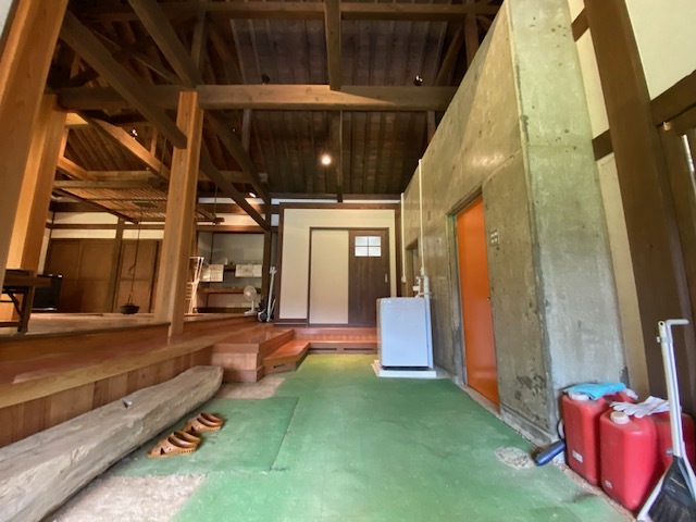 木造家屋の玄関にオレンジ色の扉や洗濯機が設置されている写真