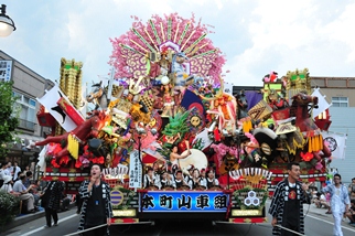 旗や花で豪華に飾られた山車が道路を移動している写真