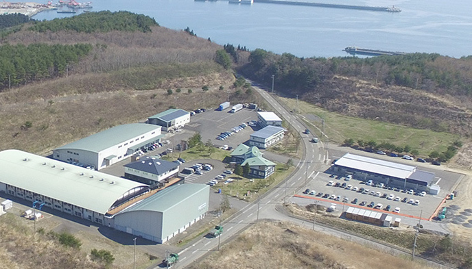 久慈港付近にある企業施設の航空写真 手間に駐車場があり奥に海が広がっている