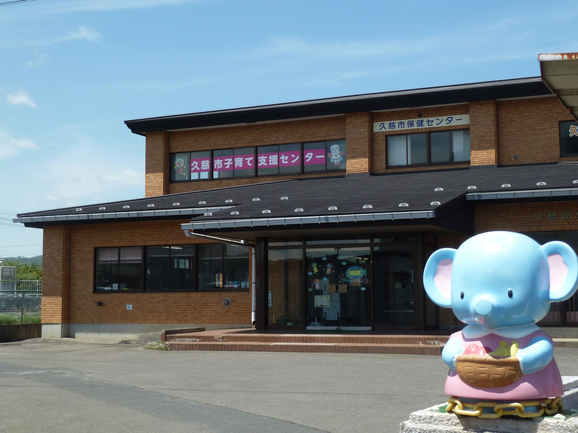 入口に水色の象のキャラクターの置物が設置された、背の低い茶色い外壁の建物の写真