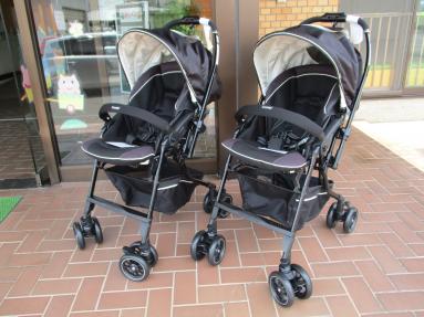 建物の入口脇に置かれた、黒い屋根付きベビーカー2台の写真