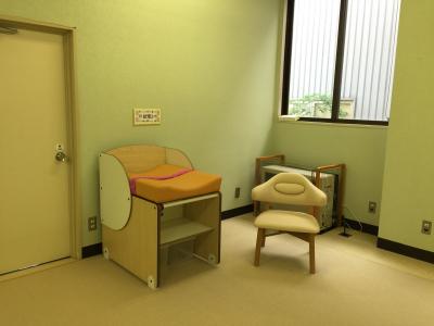 室内に設置されたおむつ交換用ベッドと、背の低い椅子の写真