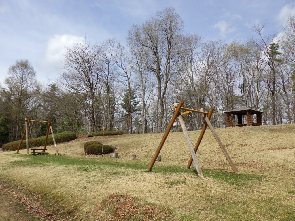 野原に木で組まれたオブジェとベンチが置かれている写真