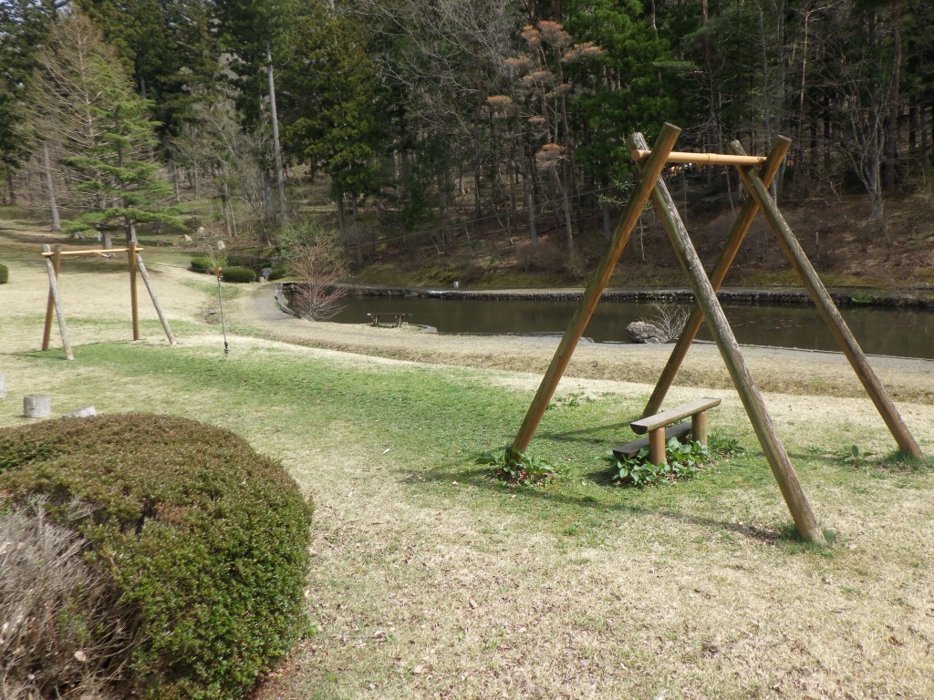 池の手前にあるベンチと木で組まれたオブジェの写真