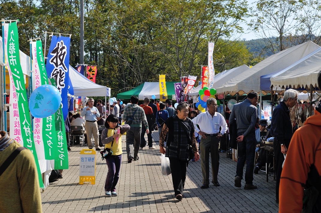 イベント用テントが並んでいる広場で大勢の人たちが歩いている写真