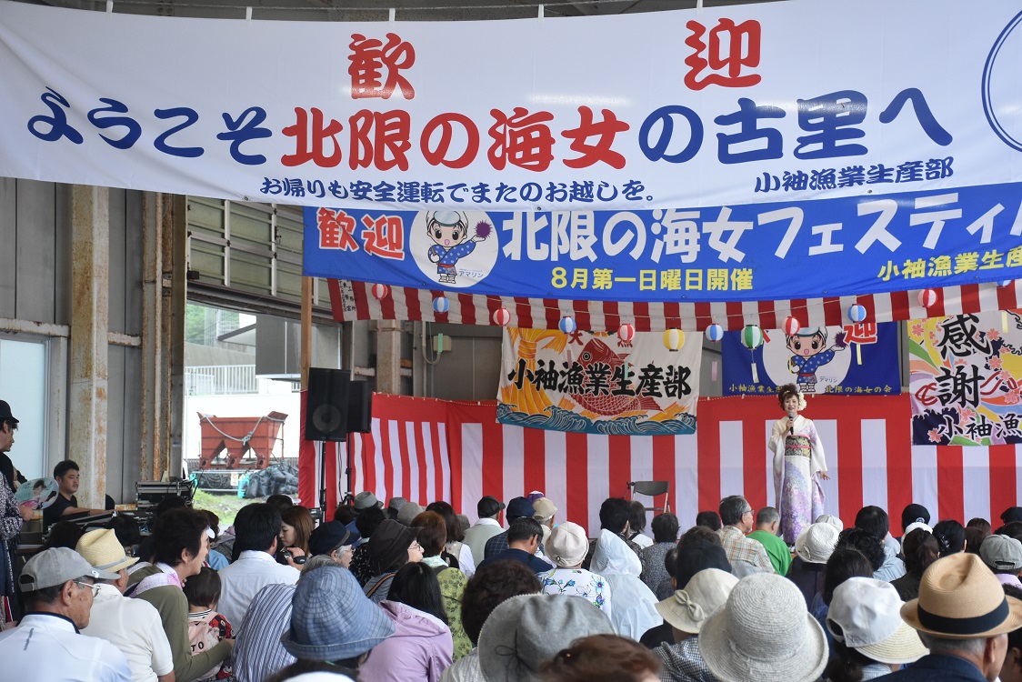 北限の海女フェスティバルの幕が複数枚ある会場にたくさんの人が集まっている写真