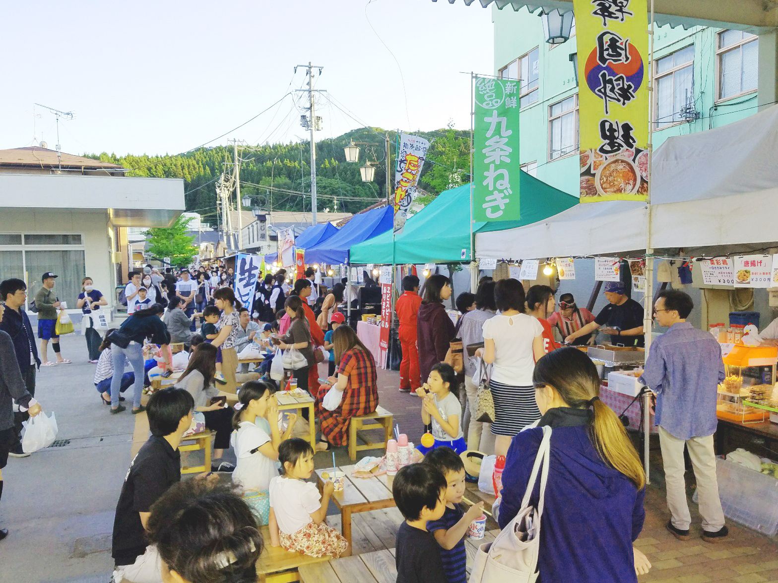 イベント用テントの前に並べられたテーブルに着席してご飯を食べている人たちの写真