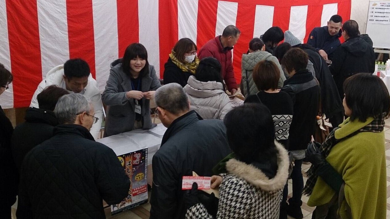 白い布をかぶせたテーブルにいる受付の人たちが来場者の対応をしている写真