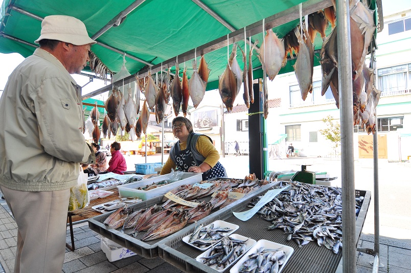 干物を中心とした屋台を運営している女性と屋台を見ている男性の写真