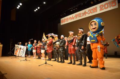 あまちゃんサミット久慈2015の幕を背景に仮装した人やマスコットキャラクターが並んでいる写真