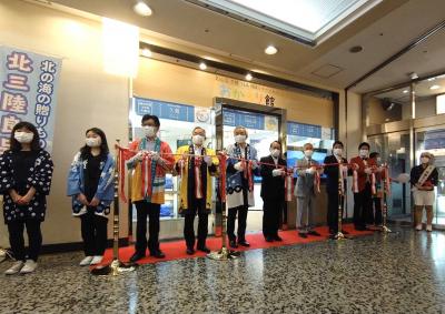 複数の男性たちが横一列に並びテープカットのテープを持っている写真