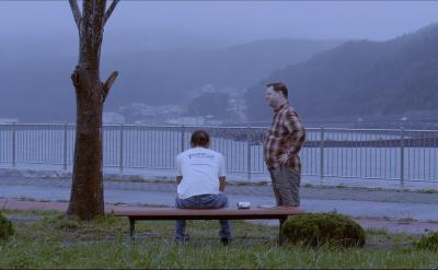 海の見える広場に設置された椅子に座る人とそばで立っている人の写真