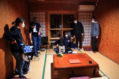 旅館の部屋の中でカメラなどの撮影器具を持って話し合いをしている人たちの写真