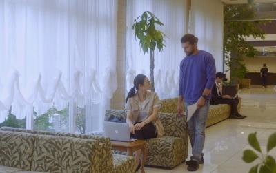 ホテルのロビーにある椅子に座っている女性と立っている男性が顔を合わせて話している写真