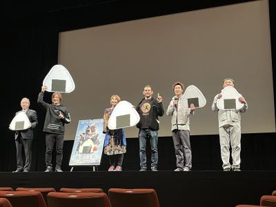 映画の上映会のステージに立った人たちがおにぎりのパネルを持っている写真