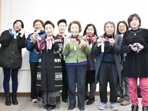 集まった女性たちがリボンを手に持って微笑んでいる写真