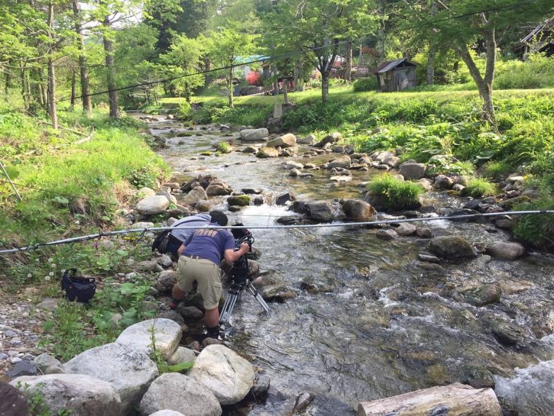 小川に足を浸けながらカメラで撮影をしている写真