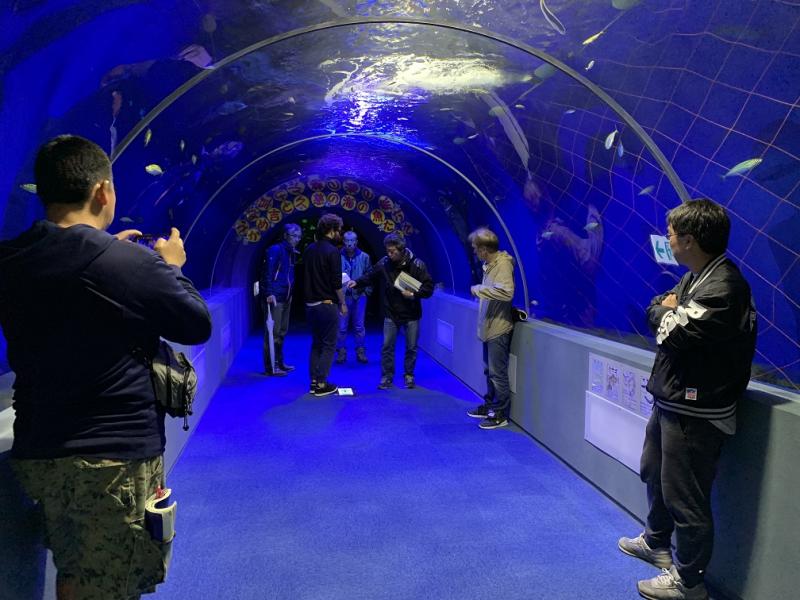 水槽がアーチ状になっている水族館の中で複数の男性が集まっている写真