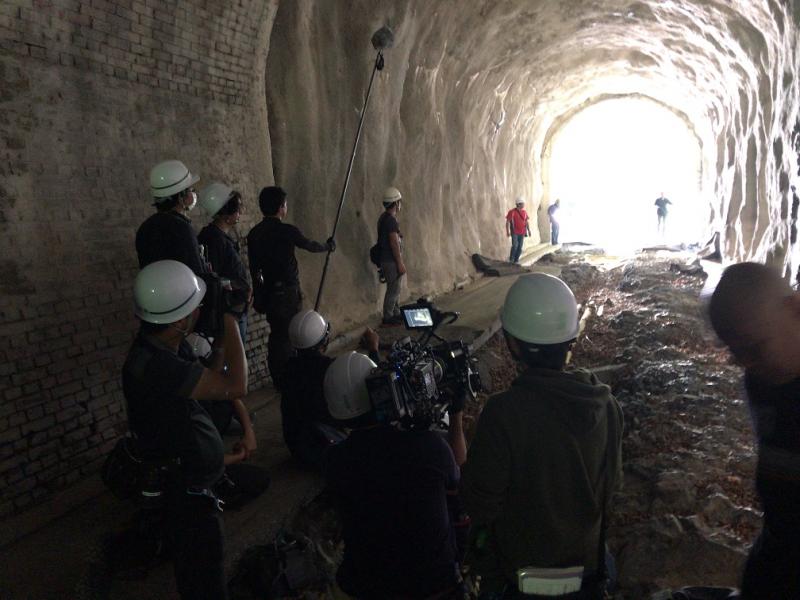 暗いトンネルの中で光の差す外に向かってカメラを回し撮影をしている写真