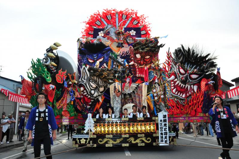 鬼の形相をした顔が複数並んでいる山車が道路を練り歩いている写真