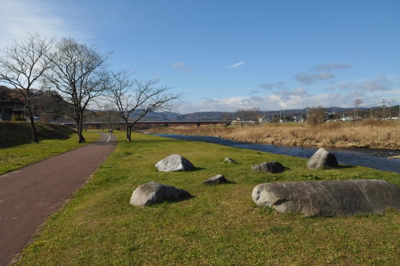 大小様々な石がまばらに置かれた芝のそばに道や川がある写真
