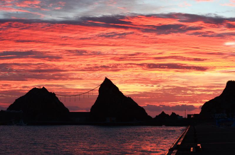 赤い夕焼けを背景に海辺の岩と岩の間で縄が掛けられている写真