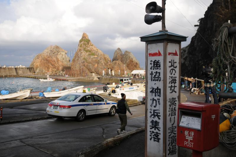 海沿いの道に漁協・袖が浜集落、北の海女素潜り実演場と書かれた看板が立てられている写真