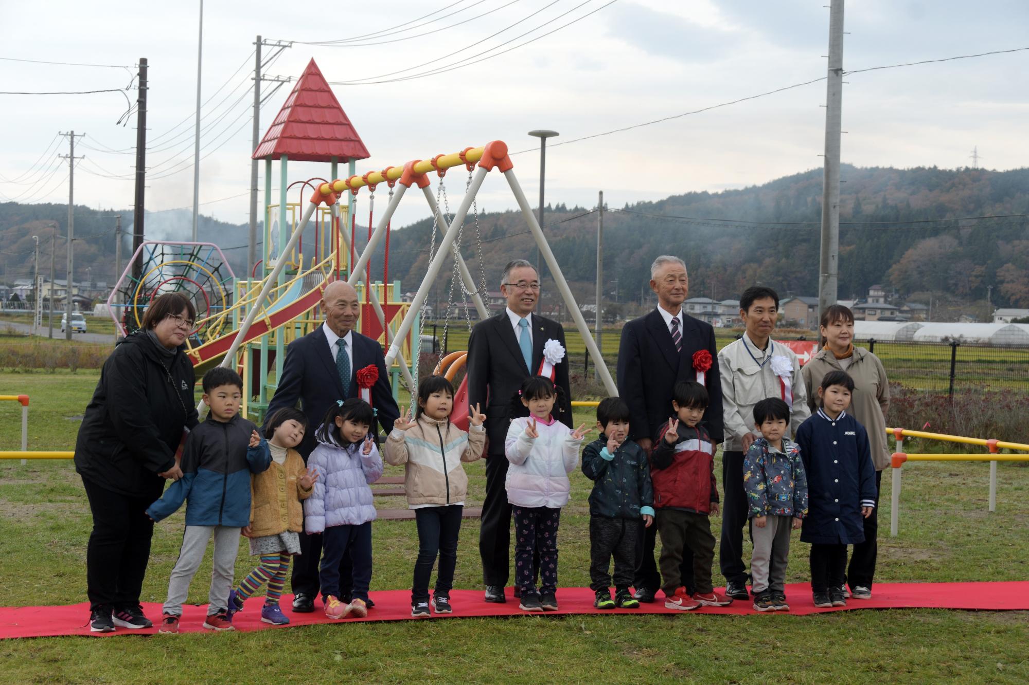 公園で9人の子供と6人の大人が並んで記念撮影をしている写真
