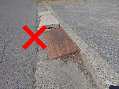 道路端の段差に鉄板が置かれている状態にバツ印が付いている写真