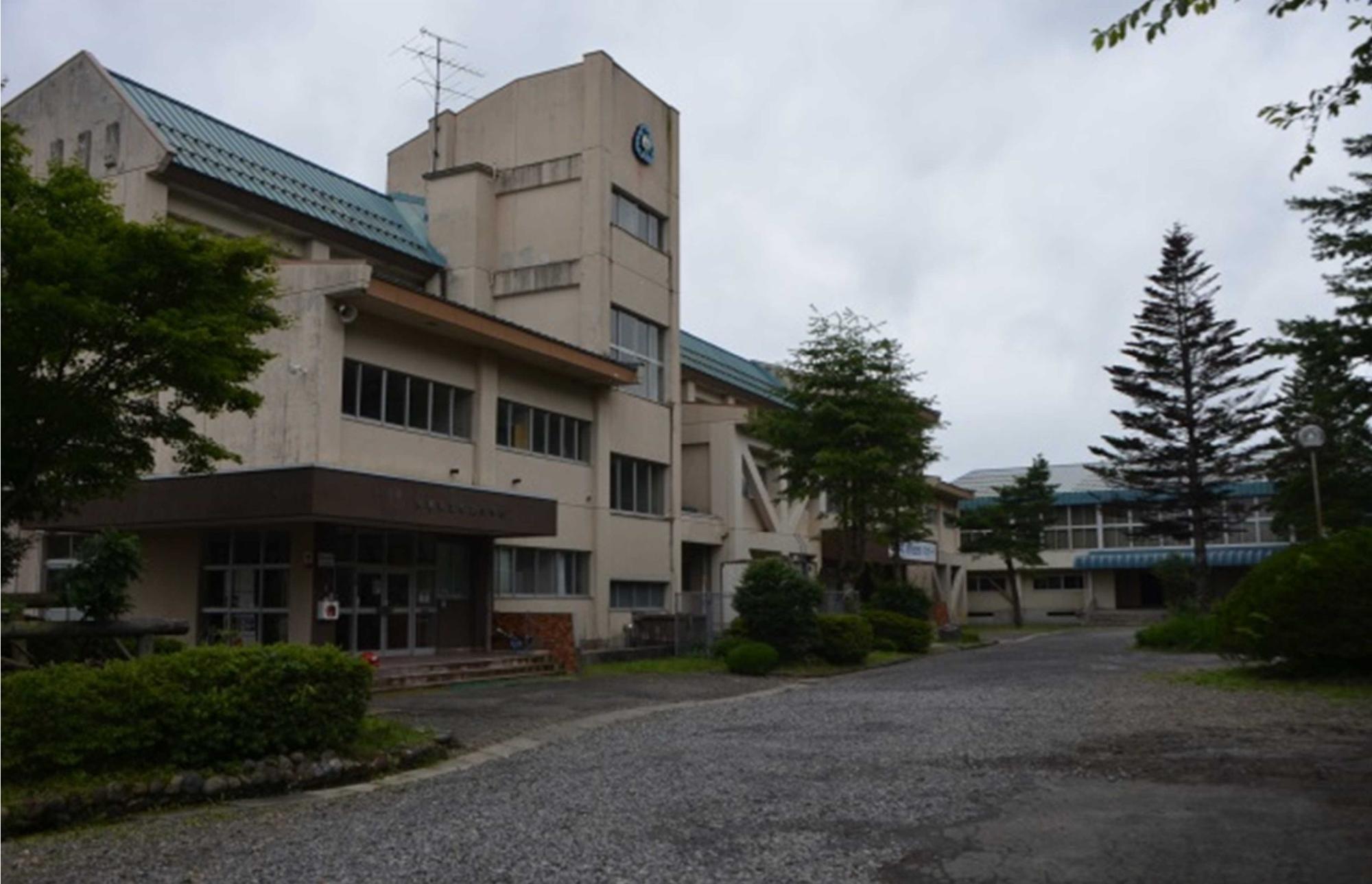 青緑色の屋根の3階建ての校舎を斜め前から見た外観の写真