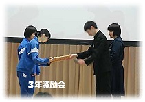 「3年激励会」と書かれた文字と、青ジャージ姿の2名が制服姿の2名から紙を受け取っている写真