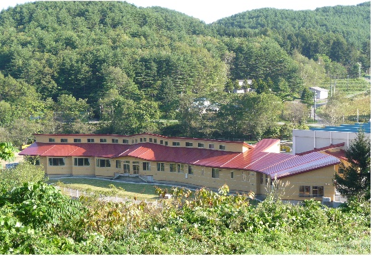 周りを山などの緑に囲まれた中に建つ、赤い屋根の校舎の写真