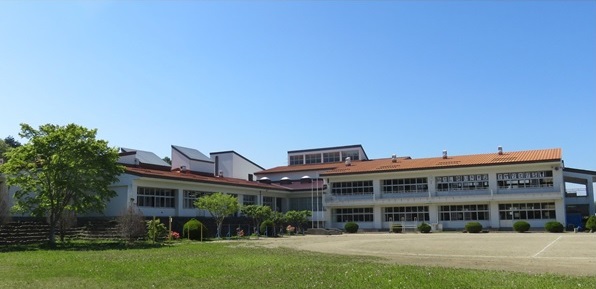 オレンジ色の屋根の2階建て校舎と校庭の写真