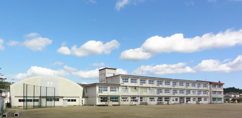 体育館の右側に3階建ての校舎が建っている学校の写真