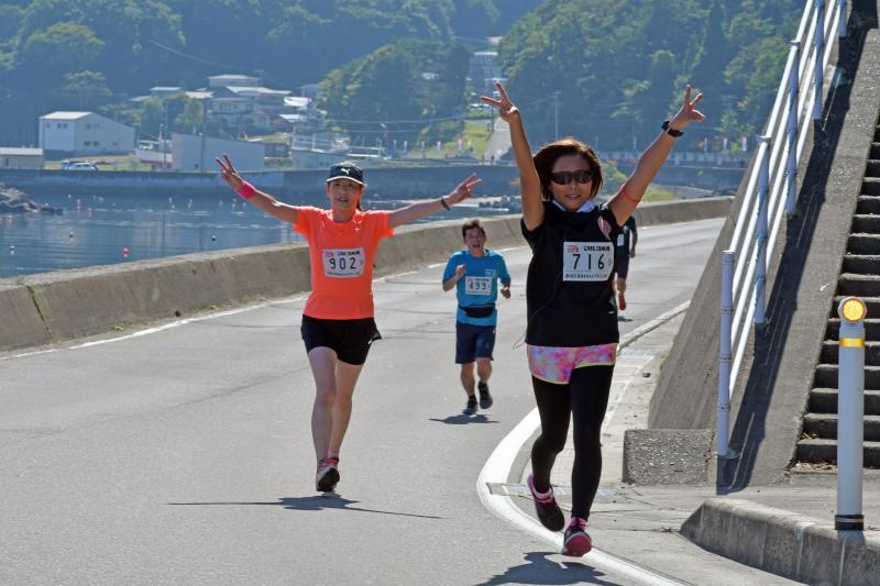 女性のマラソンランナー2人が両手をピースにし上に掲げながら走っている写真