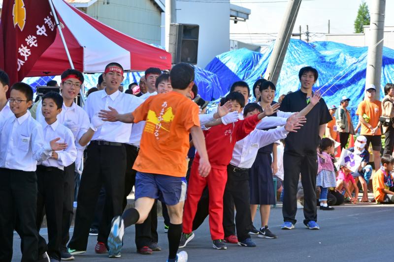 マラソンランナーが学生たちとハイタッチしながら走っている写真