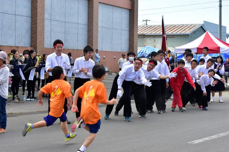 男の子2人が走っている前方で学生の男の子たちがハイタッチをするのを待ち構えている写真