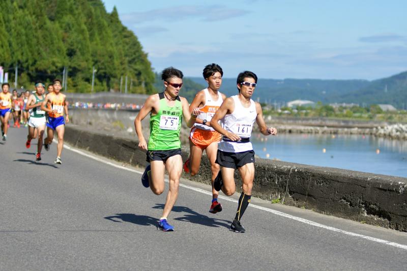 男性たちが海沿いの道路を走っている写真