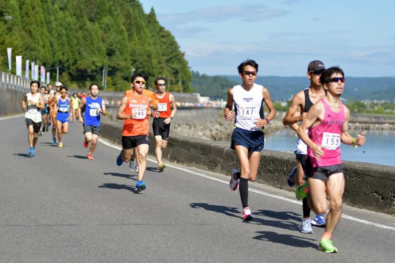マラソンランナーの男性たちが海沿いの道路を走っている写真