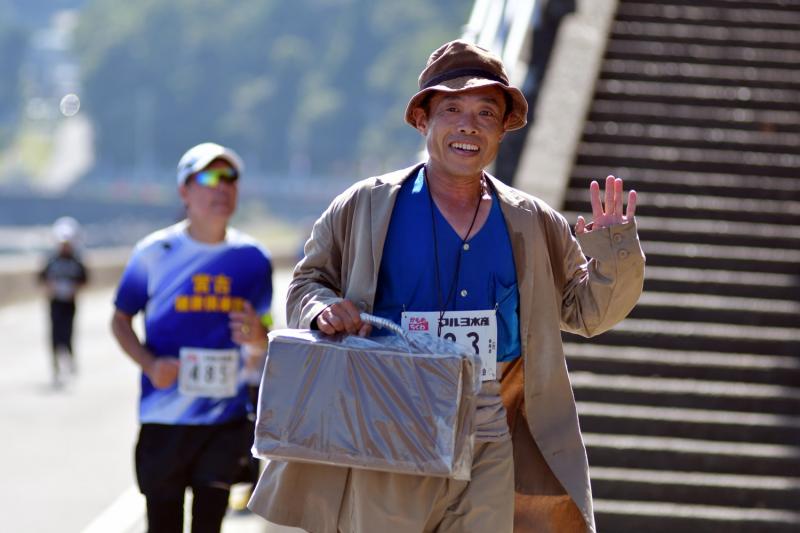 寅さんの格好をした男性が片手にカバンを持って手を振っている写真