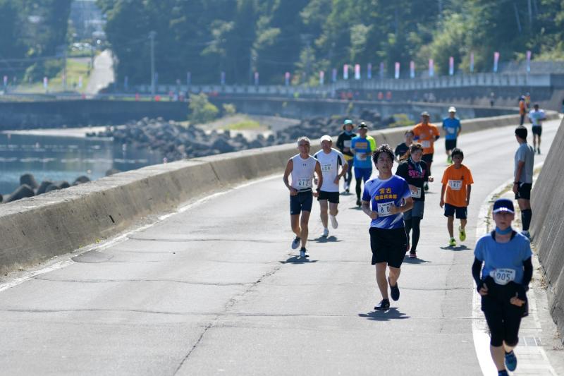 マラソンランナーたちが海沿いの道路を走ったり歩いている写真