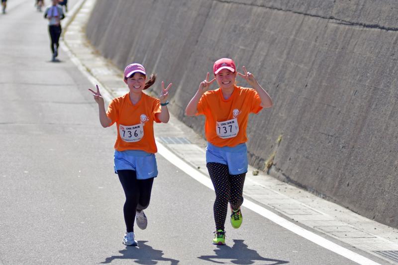 女性のランナー2人が両手でピースをしながら一緒に走っている写真